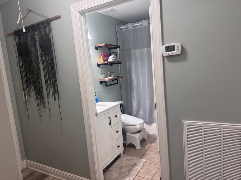 Doorway view of a bathroom with toilet, sink vanity, shelving, and gray shower curtain