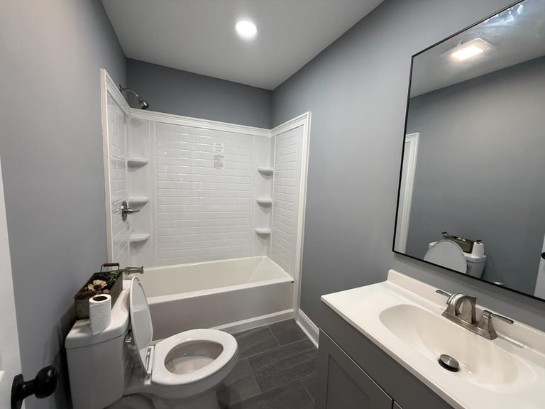Modern bathroom with white subway tile shower, toilet, white vanity sink with mirror, gray walls and dark floor