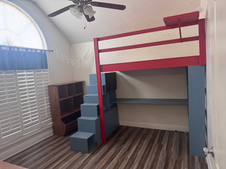 A modern loft bed with burgundy frame and blue stairs, featuring built-in shelving underneath in a bedroom with striped flooring.