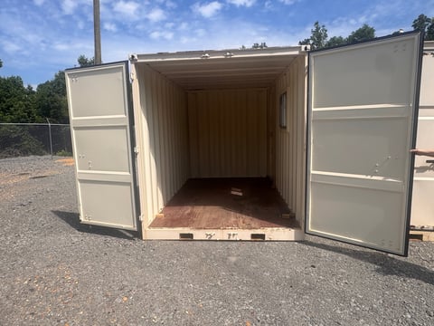 Empty shipping container with open double doors revealing the interior, parked on gravel outdoors