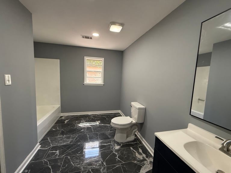Modern bathroom with gray walls, black marble flooring, white toilet, vanity sink, and large mirror