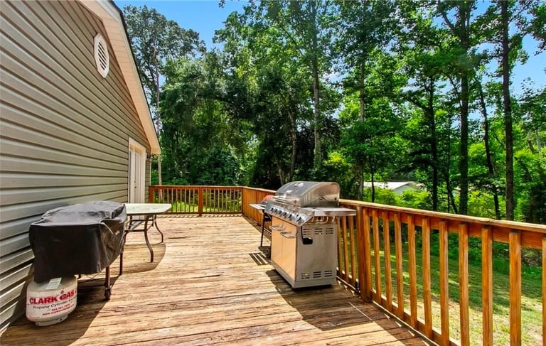 Wooden deck with grill, fire pit, and furniture overlooking wooded backyard