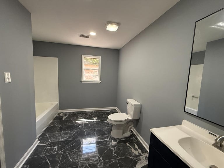 Modern bathroom with gray walls, black marble tile floor, white sink vanity, toilet, mirror, and small window