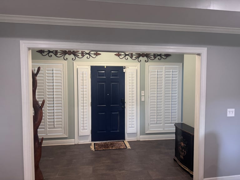 Entryway with dark hardwood floors, white shutters on either side of a dark blue front door, decorative metal hardware above the doorway
