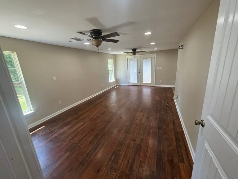 Empty room with dark hardwood floors, beige walls, ceiling fan, and glass doors leading to outdoor space