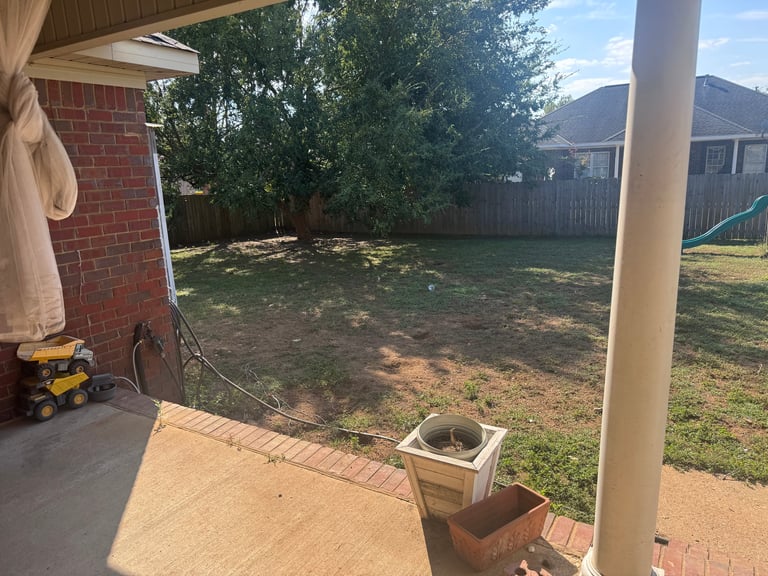 Backyard patio view with brick wall, white column, potted plants, and residential properties with wooden fence in background