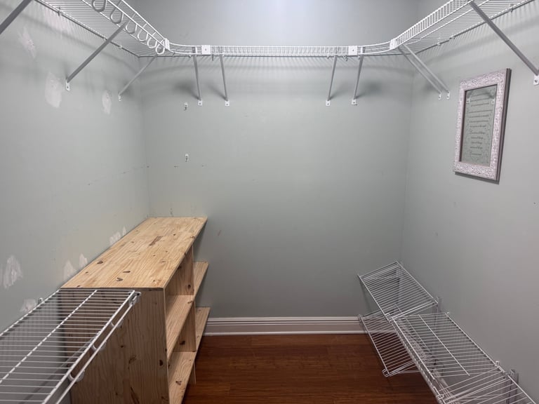 Empty walk-in closet with white wire shelving, wooden shelf unit, hardwood floor, and bright overhead lighting
