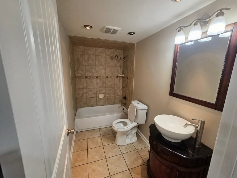 Modern bathroom with tile flooring, bathtub, toilet, vanity sink, and large mirror with overhead lighting