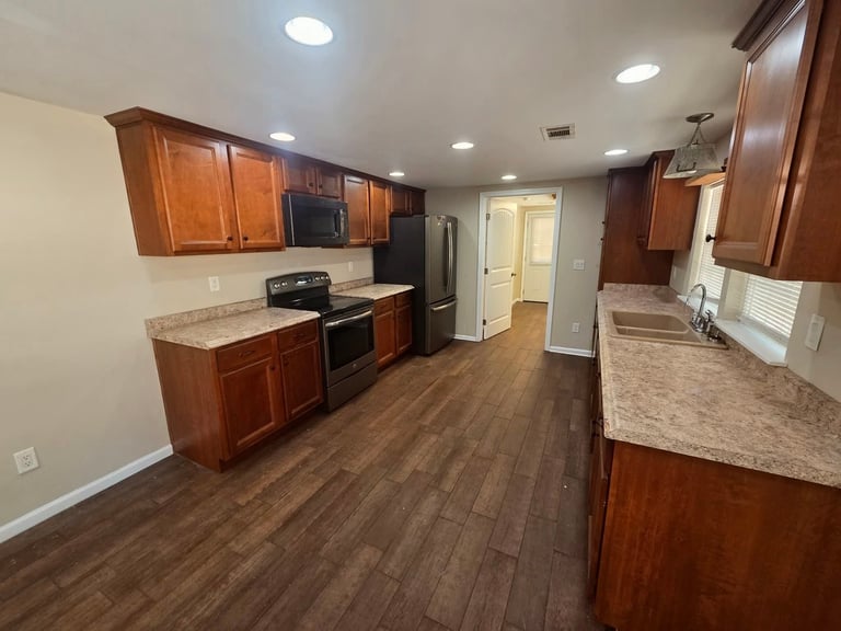 Modern kitchen with cherry wood cabinets, granite countertops, stainless steel appliances, and wood-grain flooring