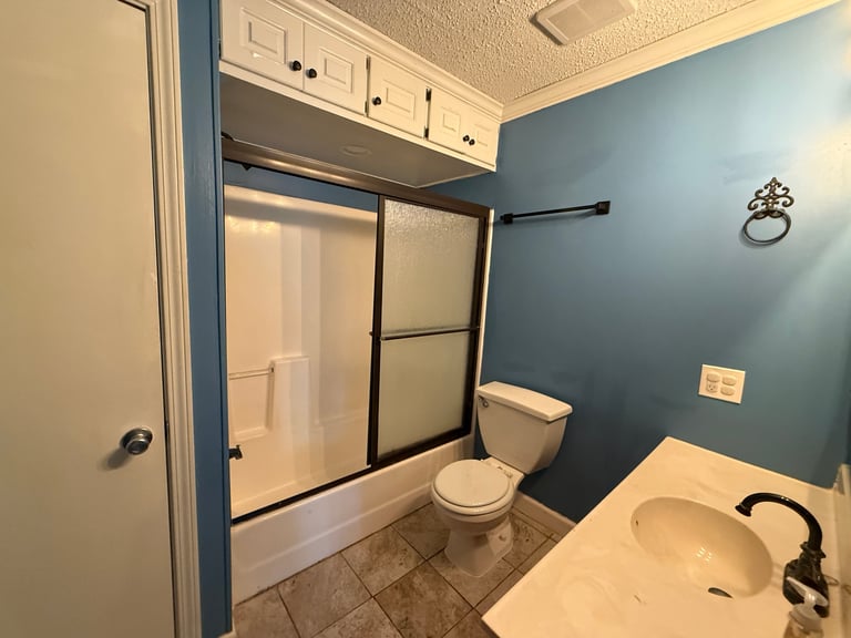 Modern bathroom with blue walls, white vanity sink, toilet, and glass-door shower enclosure with black frame