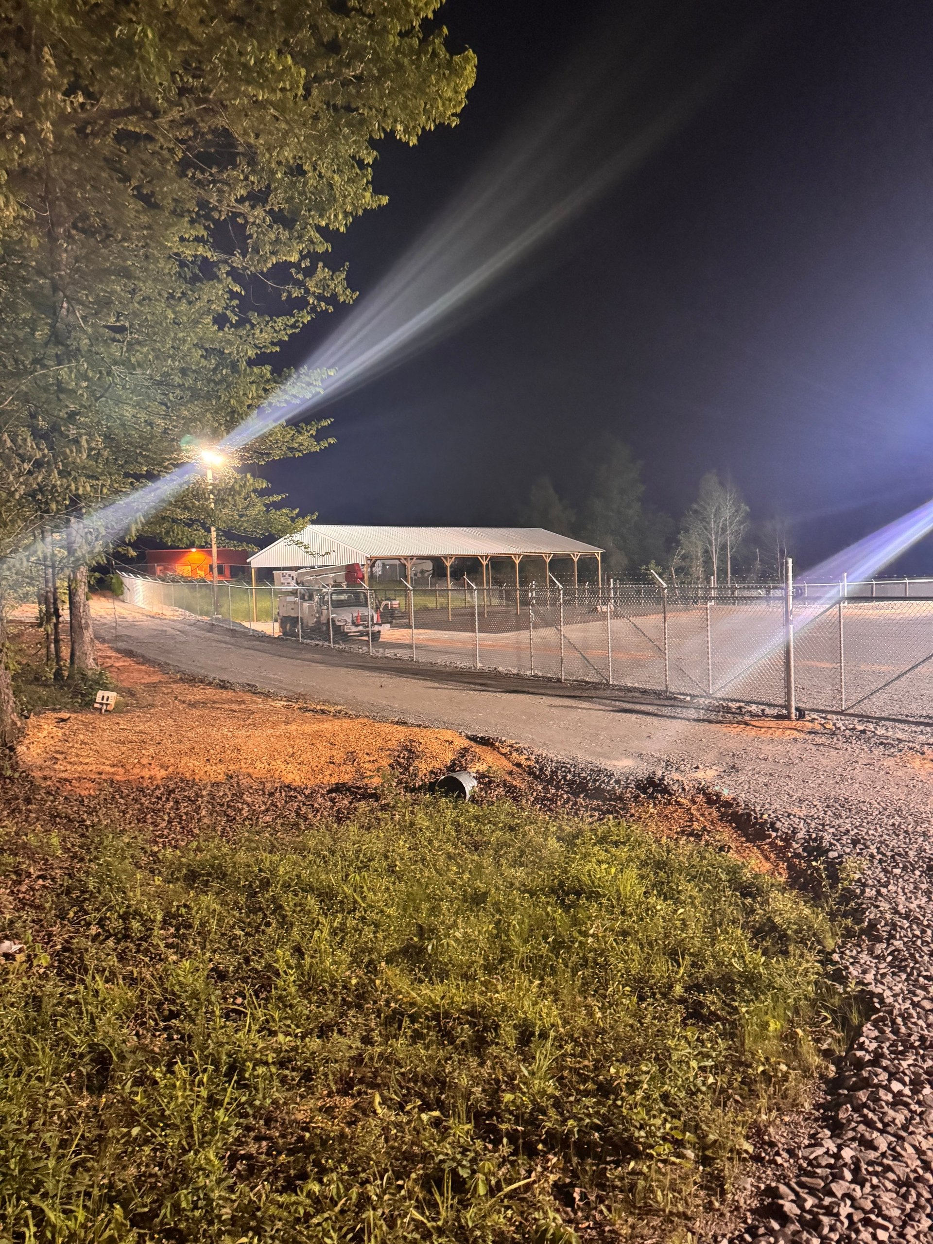 Nighttime outdoor facility with illuminated metal fencing and covered structure at Warrior RV Park