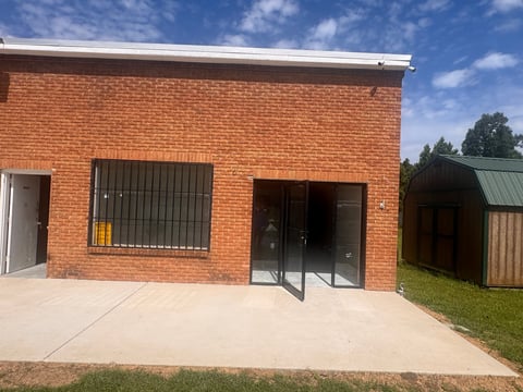 Red brick building with concrete patio, barred window, and glass doors under blue sky