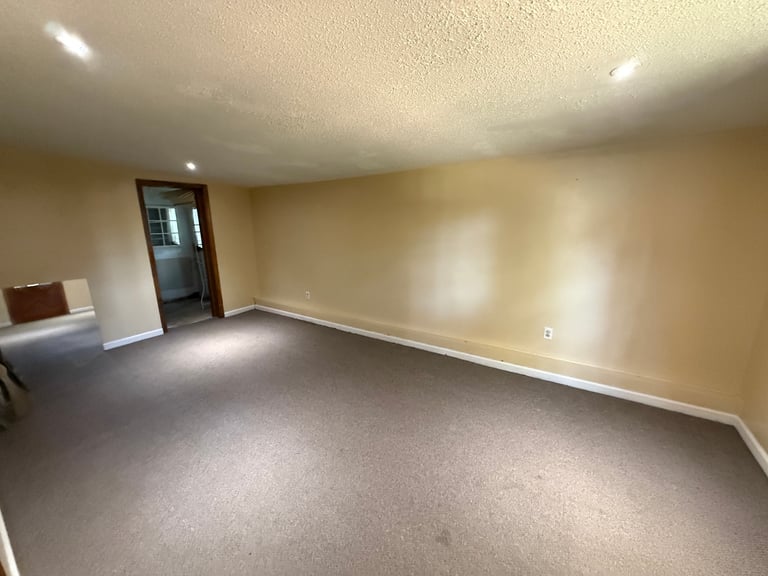 Empty room with beige walls, gray carpet, recessed ceiling lights, and dark wooden door