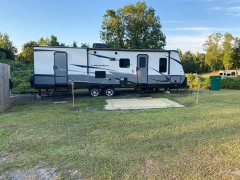 White and black travel trailer parked on grass at a campground with trees in background