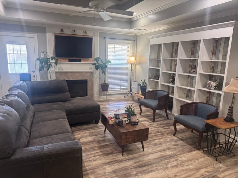 Modern living room with gray sectional sofa, fireplace with TV, white built-in shelving, and wooden coffee table on hardwood flooring