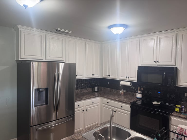 Modern kitchen with white cabinetry, black granite countertops, stainless steel appliances, and blue ceiling light fixture