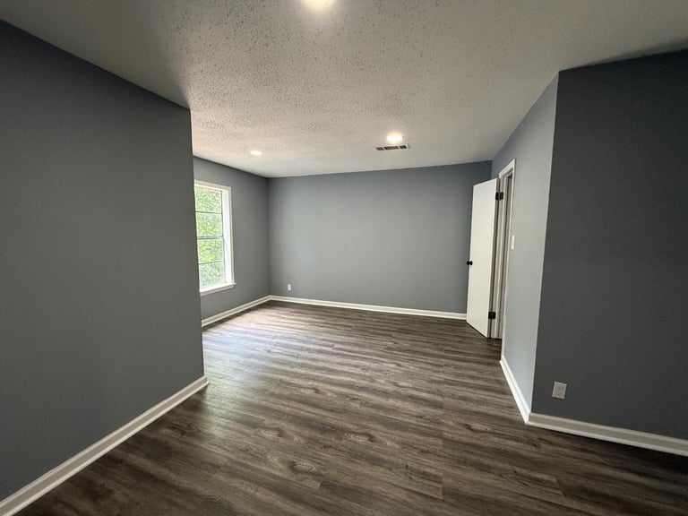 Empty room with gray walls, dark wood laminate flooring, white trim, window, and recessed ceiling lights