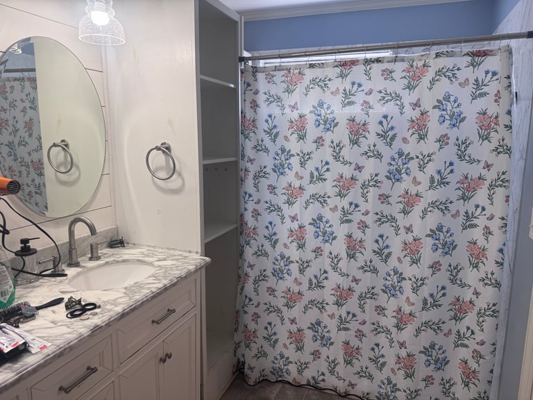 Bathroom interior with white vanity, two round mirrors, and floral patterned shower curtain with blue walls.