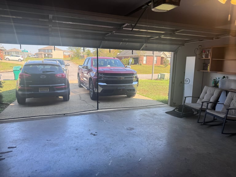 Interior view of a garage with two dark-colored SUVs parked outside and folding chairs on the right wall